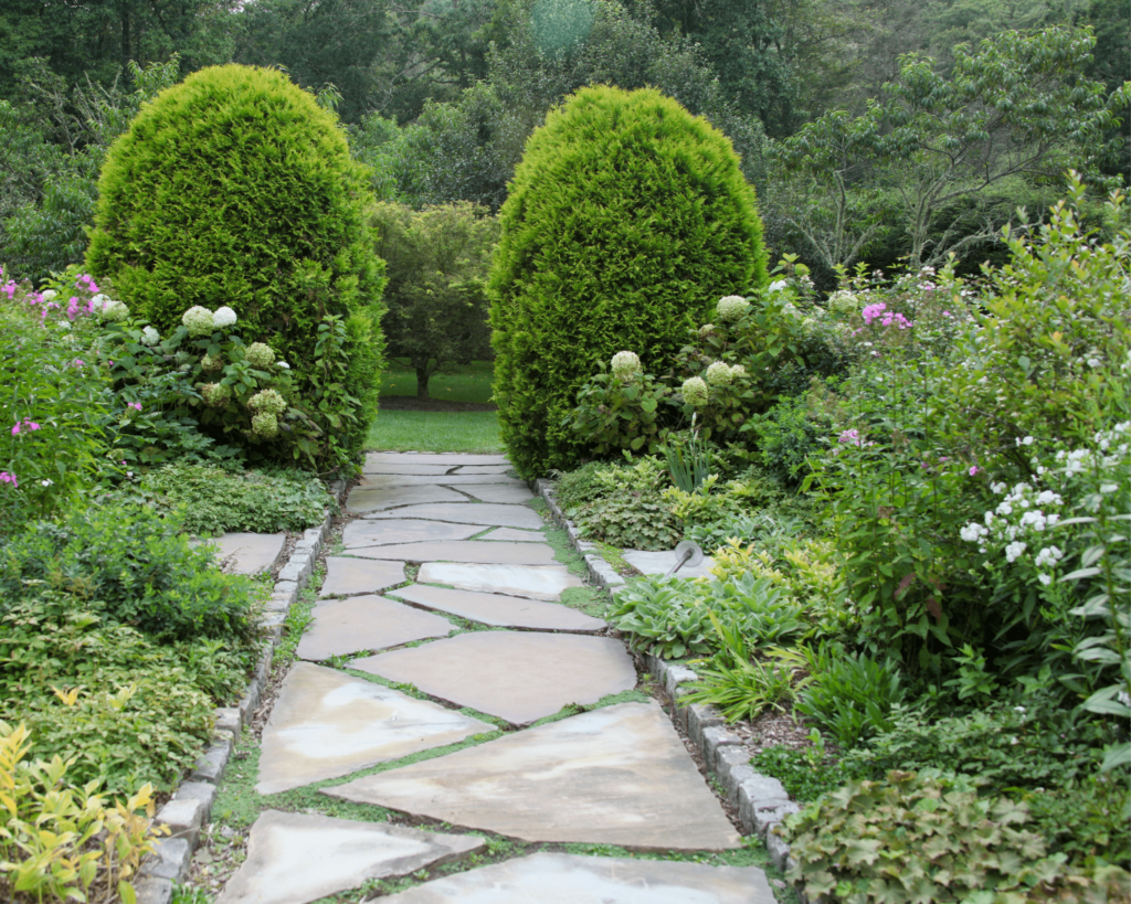 Picture of a charming stone path winding through a lush garden, bordered by vibrant plants - an example of the paths and walkways designed by Custom Creations in the Ozarks.