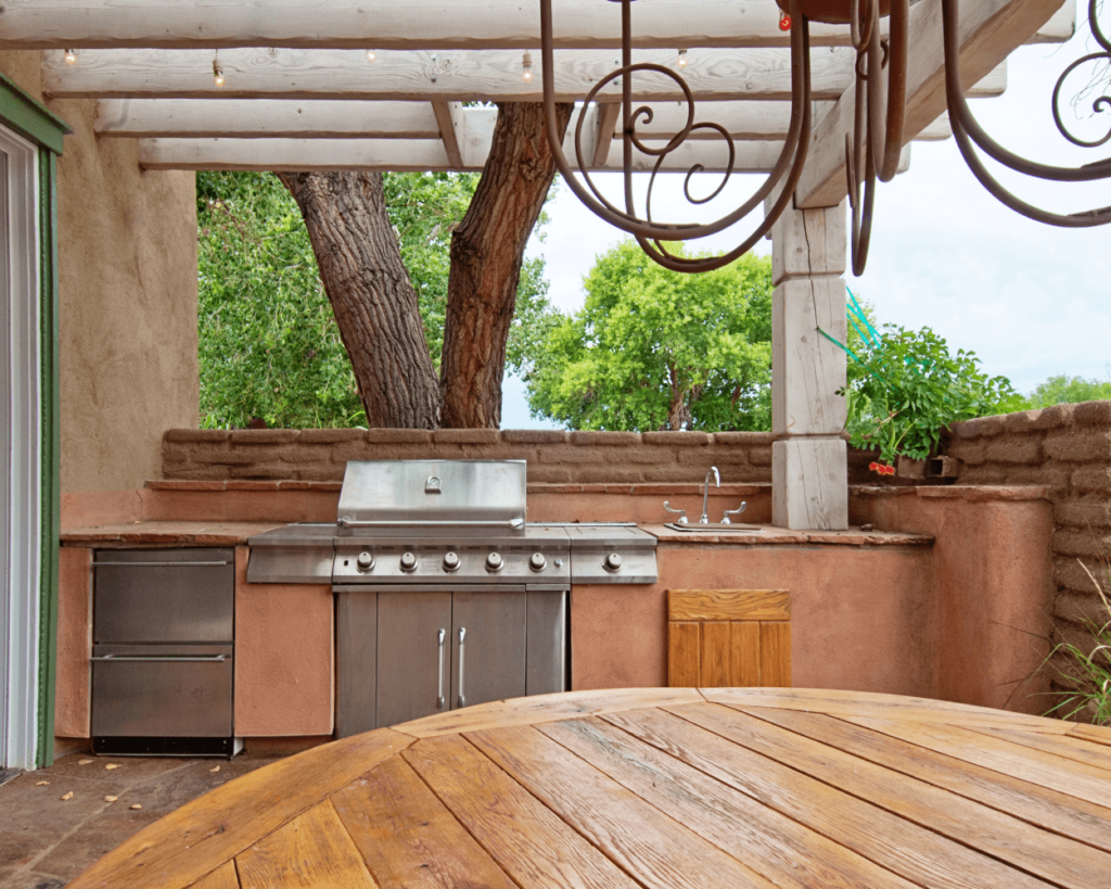 A rustic outdoor kitchen with oxidized woven steel backdrop, colorful tiles, and desert-inspired furniture, with desert plants in the background.